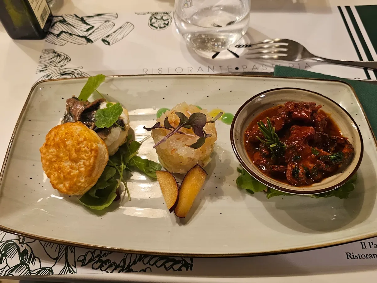 Cacciucchetto di moscardini servito in ciotola con rosmarino, accanto a baccalà e contorni
