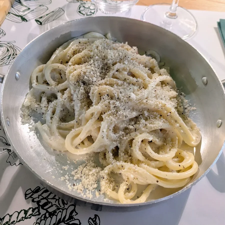 Cacio e pepe servita nel tegamino di alluminio sulla tovaglietta illustrata del ristorante