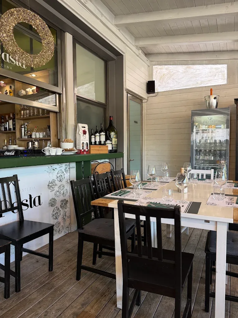 Il bancone verde del ristorante con le bottiglie di vino e i tavoli apparecchiati