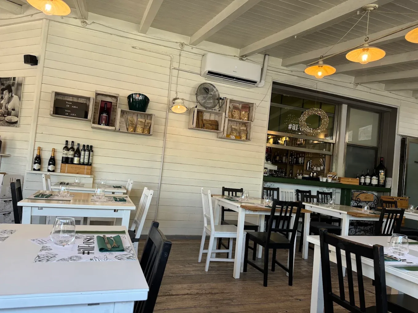La sala del ristorante: pareti in legno bianco, tavoli apparecchiati e lampade a luce calda